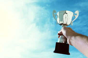 Wall Mural - man holding up a trophy cup as a winner against the blue sky. award and victory concept