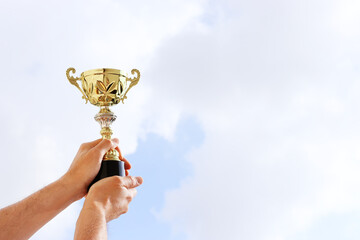Wall Mural - man holding up a trophy cup as a winner against the blue sky. award and victory concept