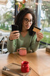 © LIGHTFIELD STUDIOS - african american woman looking at credit card while holding smartphone in cafe
