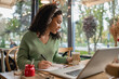 © LIGHTFIELD STUDIOS - african american woman listening podcast in headphones and holding glass with coffee near laptop in cafe