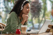 © LIGHTFIELD STUDIOS - african american woman listening podcast and looking at laptop in cafe