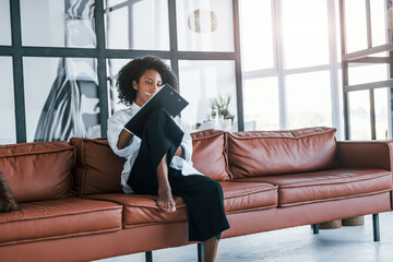 Wall Mural - Holds notepad. Young african american woman with curly hair indoors at home