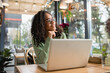 © LIGHTFIELD STUDIOS - dreamy african american woman in glasses smiling while looking away near laptop on table