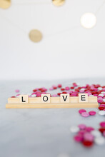 The Word Love Written In Scrabble Tiles On A Marble Counter Top Surrounded By Pink, Red, And White Chocolate Candies