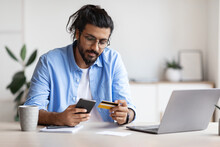 Arab Freelancer Guy Using Smartphone And Credit Card At Home, Paying Online