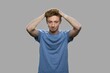 © DenisProduction.com - Frustrated teen boy on gray background. Stressed teenage guy holding hands on head.