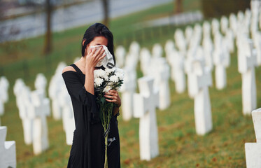 Young woman in black clothes visiting cemetery with many white crosses. Conception of funeral and death