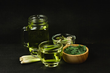 Lemon grass tea in glass and fresh lemon grass sliced and green leaf on wooden background. Healthy herbal drink concept dark tone.