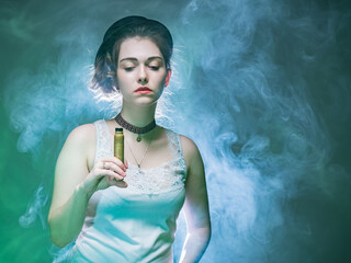 The girl with the VAPE is illuminated from behind. The woman holds a VAPE in her hand and looks down. A girl in a cloud of smoke from an electronic cigarette. The concept of vaping, vapeshop.