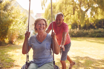 Retired Couple Having Fun With Man Pushing Woman On Garden Swing