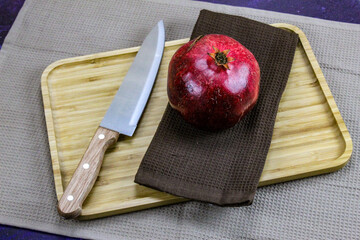 Whole pomegranate fruit on a napkin / cloth on a wooden tray on a blue background. Large red ripe pomegranate with a knife, ready to be opened. The concept of healthy life. Fruit pomegranate.