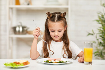 little child girl having breakfast - fried egg and orange juice in the kitchen. healthy food