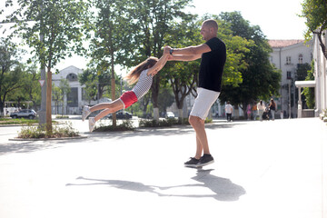 Wall Mural - Father and daughter take fun outdoor in the street . Man throws up the girl to sky. The kid laughing and imagines what is flying.