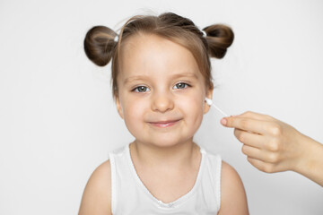 Close up of mother hand, cleaning ear of pretty little 3 years old baby girl with cotton swab. Studio horizontal shot on isolated white background. Hygiene, skincare and ear cleaning