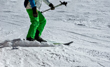 Closeup A Man Is Skiing On A Slope In Green Ski Pants Snow Is Breaking Out From Under The Skis