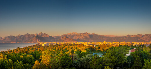 Wall Mural - Panoramic bird view over Mediterranean seacoast, mountains, beach and modern resort hotels at Antalya touristic city center during warm sunset, Antalya, Turkey.