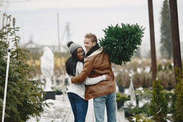 Winter concept. Guy in a brown coat. Salesman of Christmas Tree. International couple.