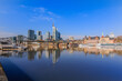 Financial district of Frankfurt in sunshine. Skyline commercial buildings and bridge over the river Main with reflections. Ships at the moorings and historical buildings under blue sky