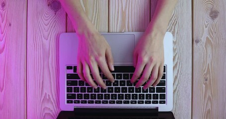 Poster - Woman’s hands typing on laptop keyboard in purple light. View from above. Remote work concept image. 4K video