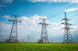 © es0lex - High voltage lines and power pylons in a flat and green agricultural landscape on a sunny day with clouds in the blue sky. Cloudy and rainy. Wheat is growing