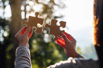 closeup image of a woman holding and putting a piece of wooden jigsaw puzzle together in the outdoor