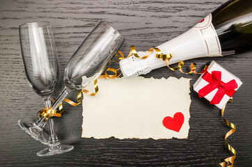 Two glasses, a bottle of champagne, a gift box, heart, a note sheet on a dark background, top view with copy space. Concept of Valentine's day, birthday, marriage proposal