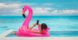 © Maridav - Relaxing woman floating in flamingo inflatable swimming pool toy at luxury resort using mobile phone sunbathing. Caribbean travel vacation hotel lifestyle.