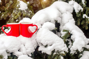 two heart shaped mugs with tea on the background snow-covered spruce
