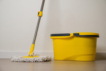 Yellow mop and bucket on the wooden floor in the living room. Home cleaning equipment yellow color.