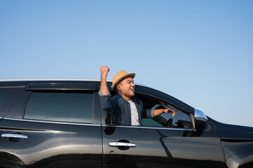 A young Asian man drives a car on a clear day. With beautiful blue sky. He driving to travel by car.