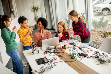 Wall Mural - Happy kids with their African American female science teacher with laptop programming electric toys and robots at robotics classroom