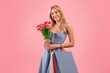 Portrait of pretty young lady with bouquet of tulips and gift bags shopping for spring holiday, pink studio background