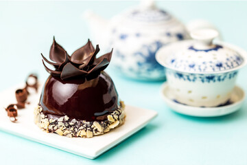 Chocolate sphere with almonds French pastry on white plate, aside Chinese teapot over light blue background.