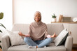 © Prostock-studio - Stress management concept. Peaceful young lady in hijab meditating with closed eyes on sofa at home