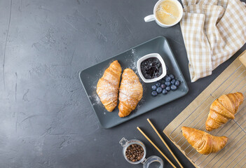 Croissants with powdered sugar and blueberries on a black plate. Top view with space for text.