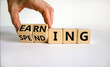 Earning or spending symbol. Businessman hand turns cubes and changes the word 'spending' to 'earning'. Beautiful white background, copy space. Business and earning or spending concept.