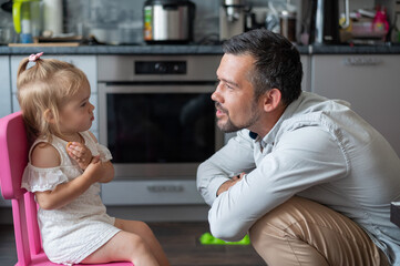 A cute little girl feeds cookies to her dad in the kitchen