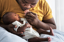 An African American Father Kissing Hand,  His 12-day-old Baby Newborn Son Lying In Bed In A White Bedroom,with Happy, Concept To African American Family And Newborn