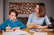 © arthurhidden - Aunt and nephew do homework together. Women explain kid writes in notebook. Schoolboy studying at home. Family relationships, primary education, childhood