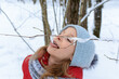 Girl licking snow from tree twigs in forest. Young girl with tongue out eating snow from branches in winter forest