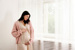 Young beautiful woman on second trimester of pregnancy. Close up of pregnant female in pink oversized knitted sweater with arms on her round belly. Expecting a child concept. Background, copy space.