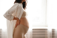 Portrait Shot Of Young Beautiful Woman On Second Trimester Of Pregnancy. Close Up Of Pregnant Female In Yoga Pants With Arms On Her Round Belly. Expecting A Child Concept. Background, Copy Space.