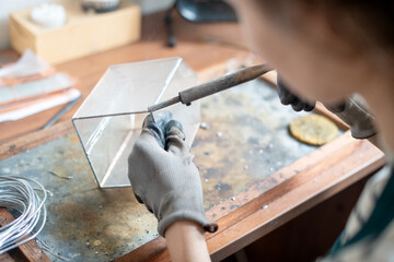 The girl works with a soldering iron in the workshop, connecting parts of the glass with foil and makes a cloche cap for decorative use.