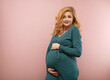 © rubchikova - Portrait of a beautiful pregnant woman in a green dress on a pink background