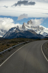 Canvas Print - Asphalted road with the peaks of a rocky and snowy mountain on the horizon. Fitz Roy mountain in Argentina vertical Photograph