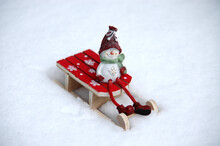 Funny Smiling Snowman In Red Boots And A Red Hat Sitting On The Red Sledge Decorated By Snowflakes Standing On The Snow