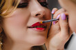 © Miramiska - Stylist paints lips of woman with red lipstick. Lip makeup close up. Professional makeup for a girl in salon. Model at the photosession.