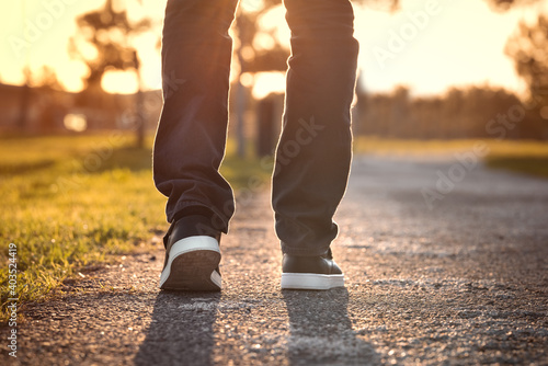 Plakat Close up of walking man at sunset in the park. Walking outdoors. Closeup on shoe, taking a step