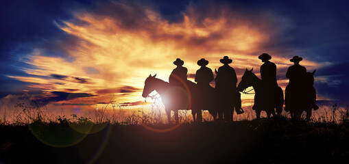 Group of cowboys on horseback at sunset