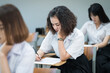 © EduLife Photos - Selective focus of the teenage college students sit on lecture chairs do final examination and write on examination paper answer sheets in the classroom. University students in uniform in classroom.